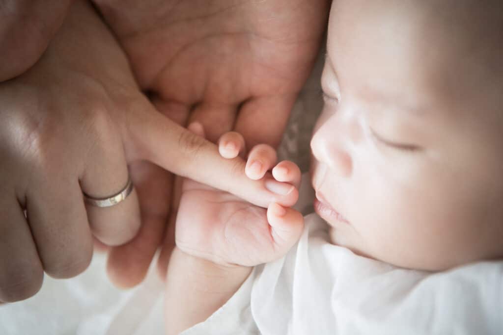 ママの指を握る寝ている赤ちゃん